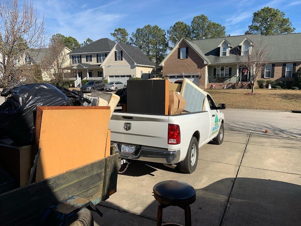 White pickup truck loaded with furniture and bags in a residential driveway on a sunny day.