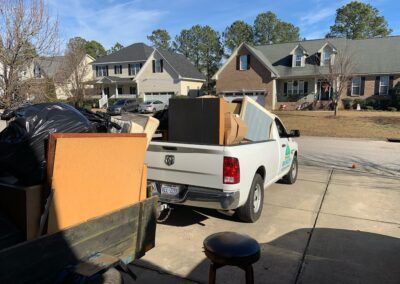 White pickup truck loaded with debris in a residential driveway. Houses in the background.
