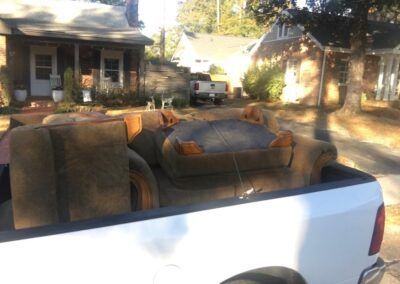 Couch pieces loaded in a white pickup truck on a residential street with houses in the background.