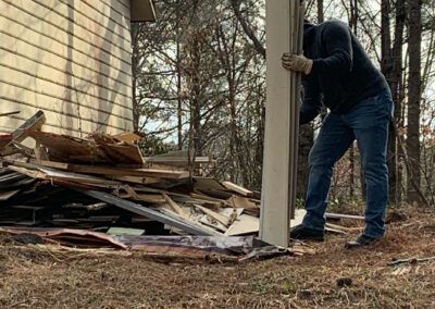 Person leans against a cream-colored post, debris and a building visible nearby.