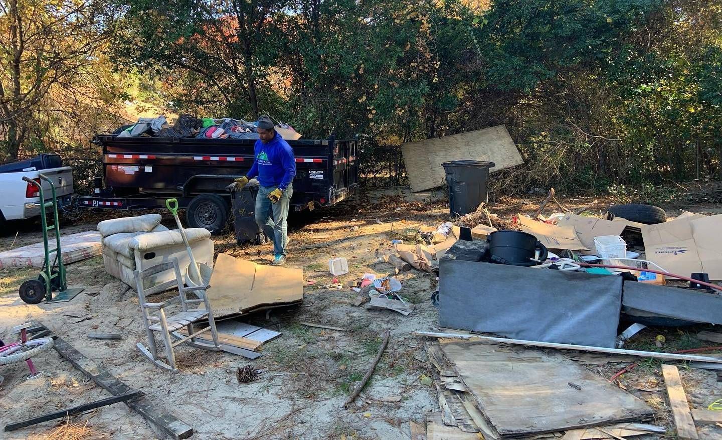 Person loading debris into a trailer; scattered trash, tools, and materials outdoors.