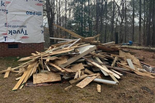Pile of construction debris in front of a partially built brick structure with Tyvek wrap.