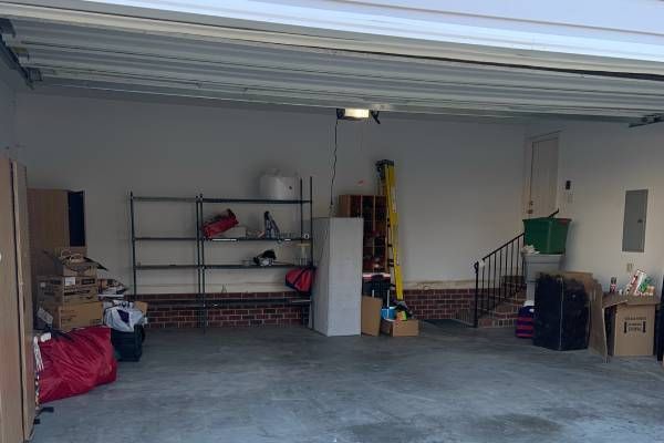 Garage interior with various items including shelves, boxes, and a ladder. Concrete floor, brick wall bottom.