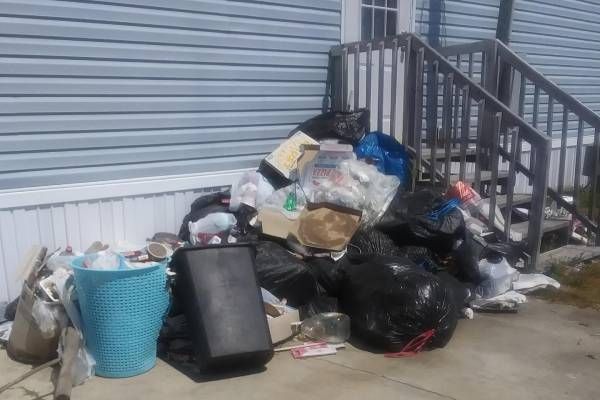 Pile of trash bags, baskets, and debris by a house's entrance.
