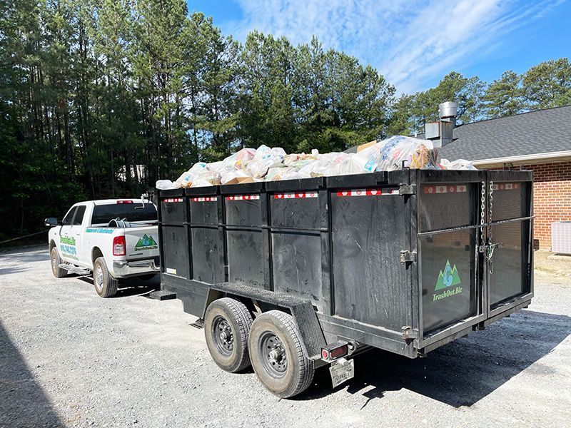White truck towing a black trailer filled with debris, parked outdoors on a sunny day.