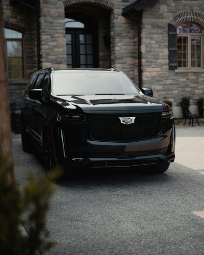 A black cadillac escalade is parked in front of a brick house.