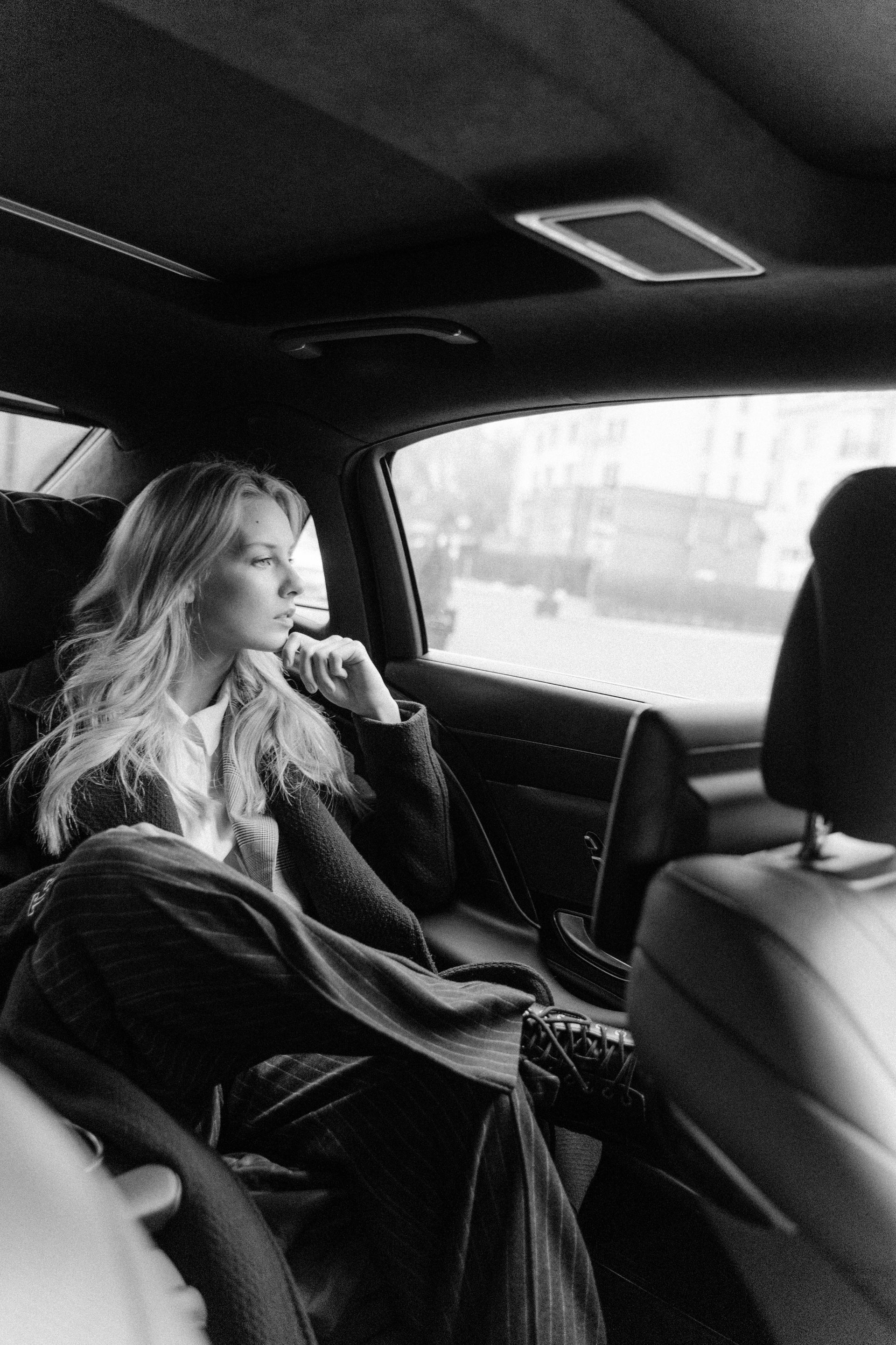 A woman is sitting in the back seat of a car looking out the window.