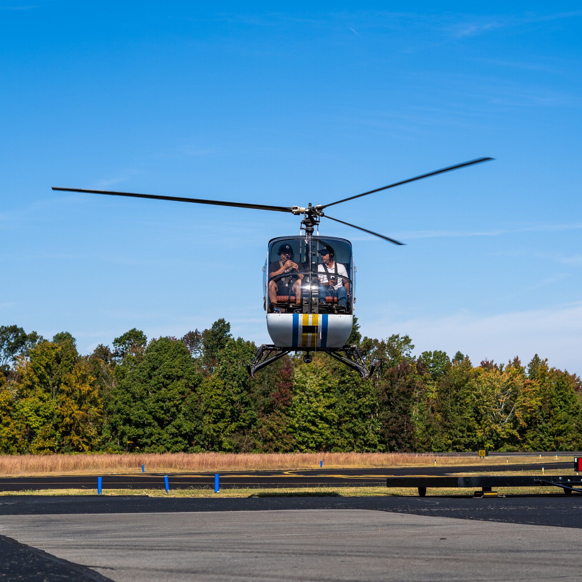 A helicopter is flying over a field with trees in the background