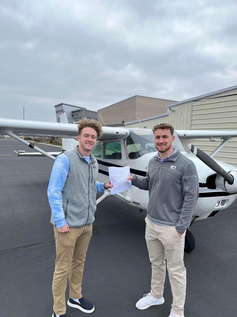 Two men are shaking hands in front of a small plane.