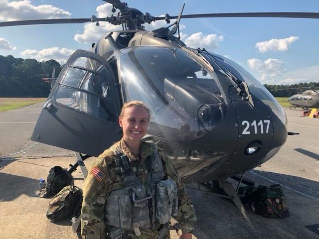 A woman in military uniform is standing in front of a helicopter with the number 1117 on it.