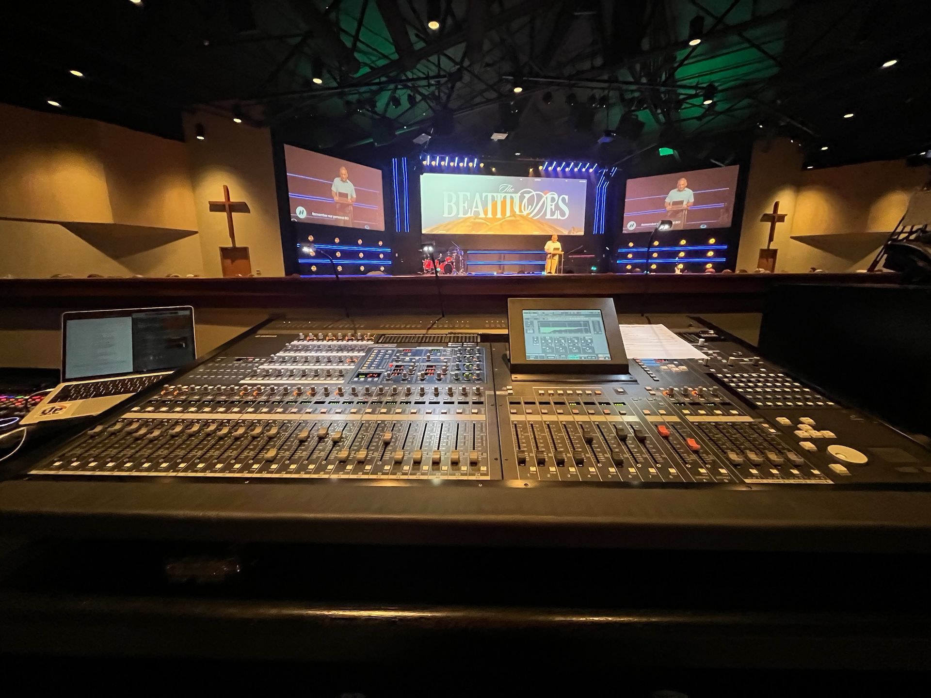 Soundboard controls in front of a church stage with screens and crosses.
