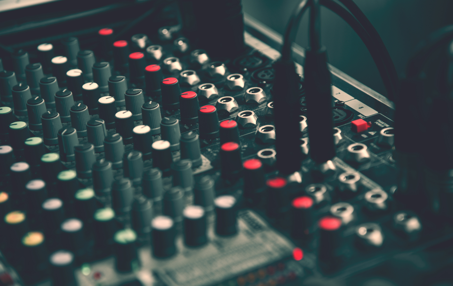 Close-up of a sound mixer with multiple knobs and buttons, some lit in red.