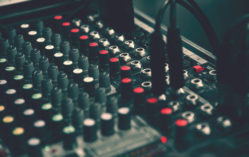Close-up of a sound mixer with multiple knobs and buttons, some lit in red.