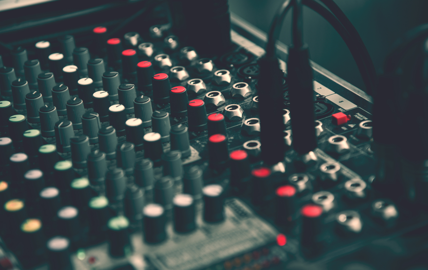 Close-up of a sound mixer with multiple knobs and buttons, some red, in a dimly lit setting.