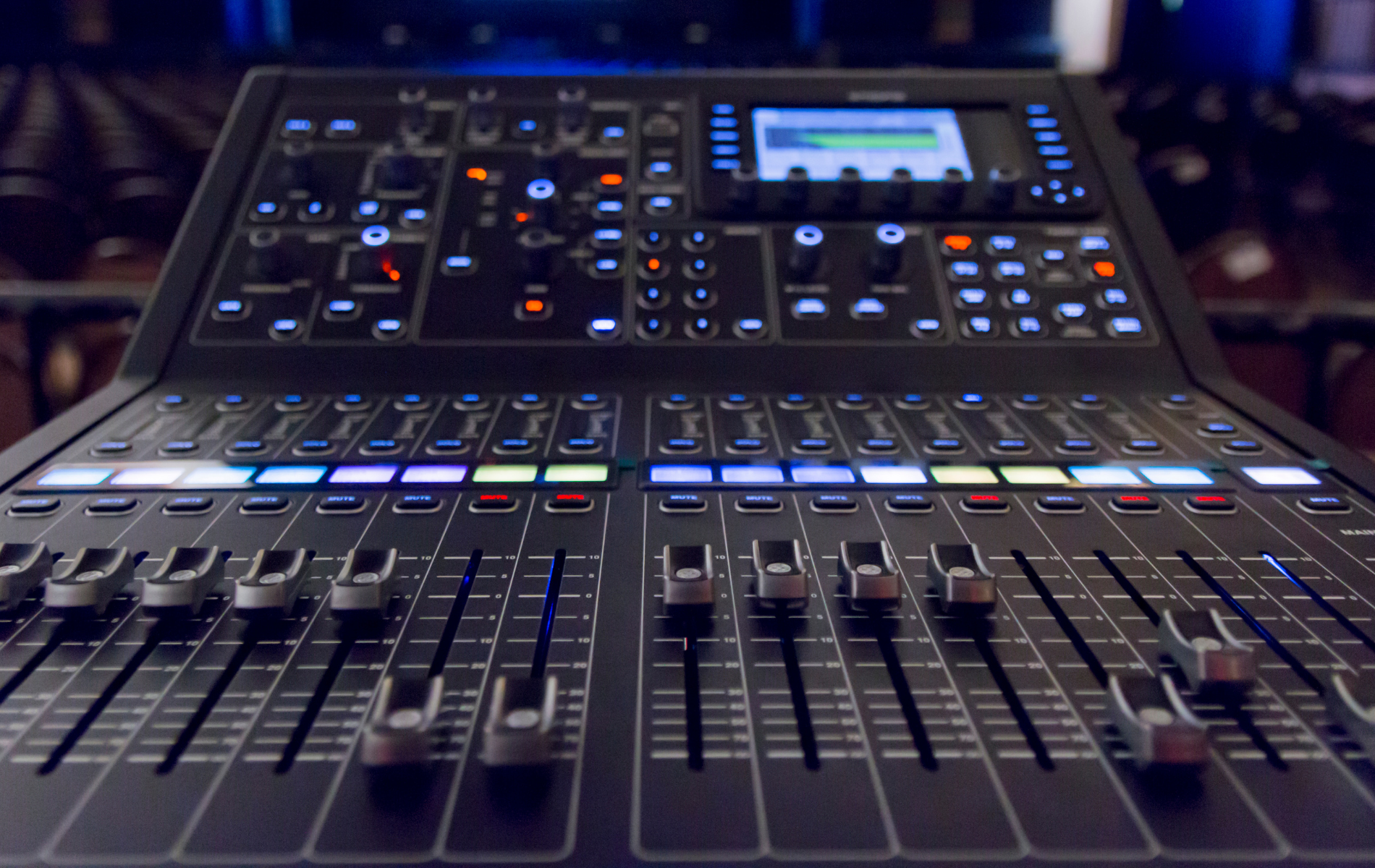 Black audio mixing console with illuminated controls and sliders.