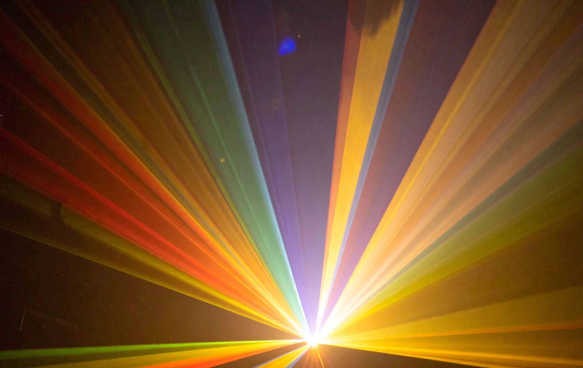 Colorful laser beams radiating from a bright central point, filling a dark space.