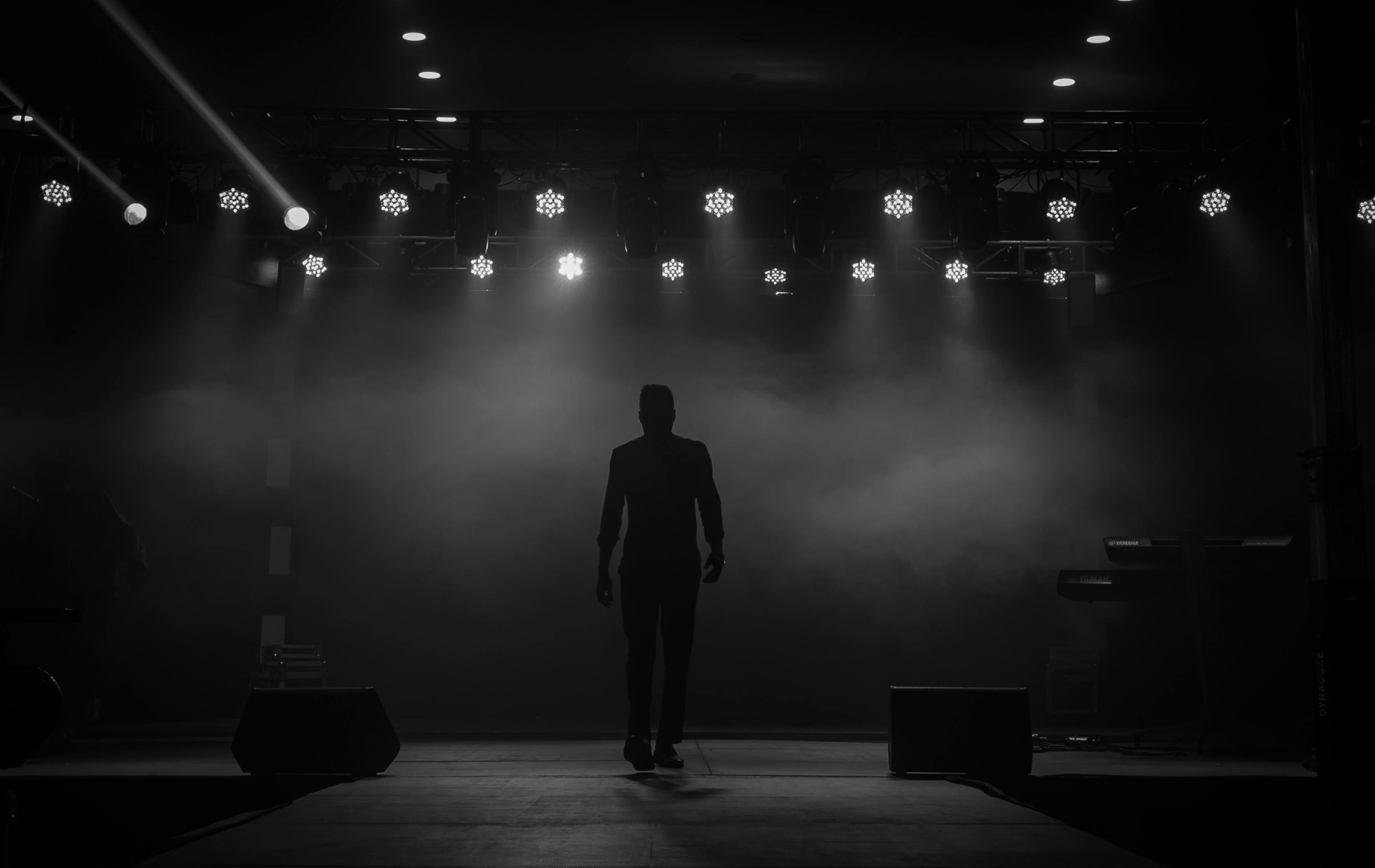 Silhouette of a person walking towards bright stage lights in a dark room.