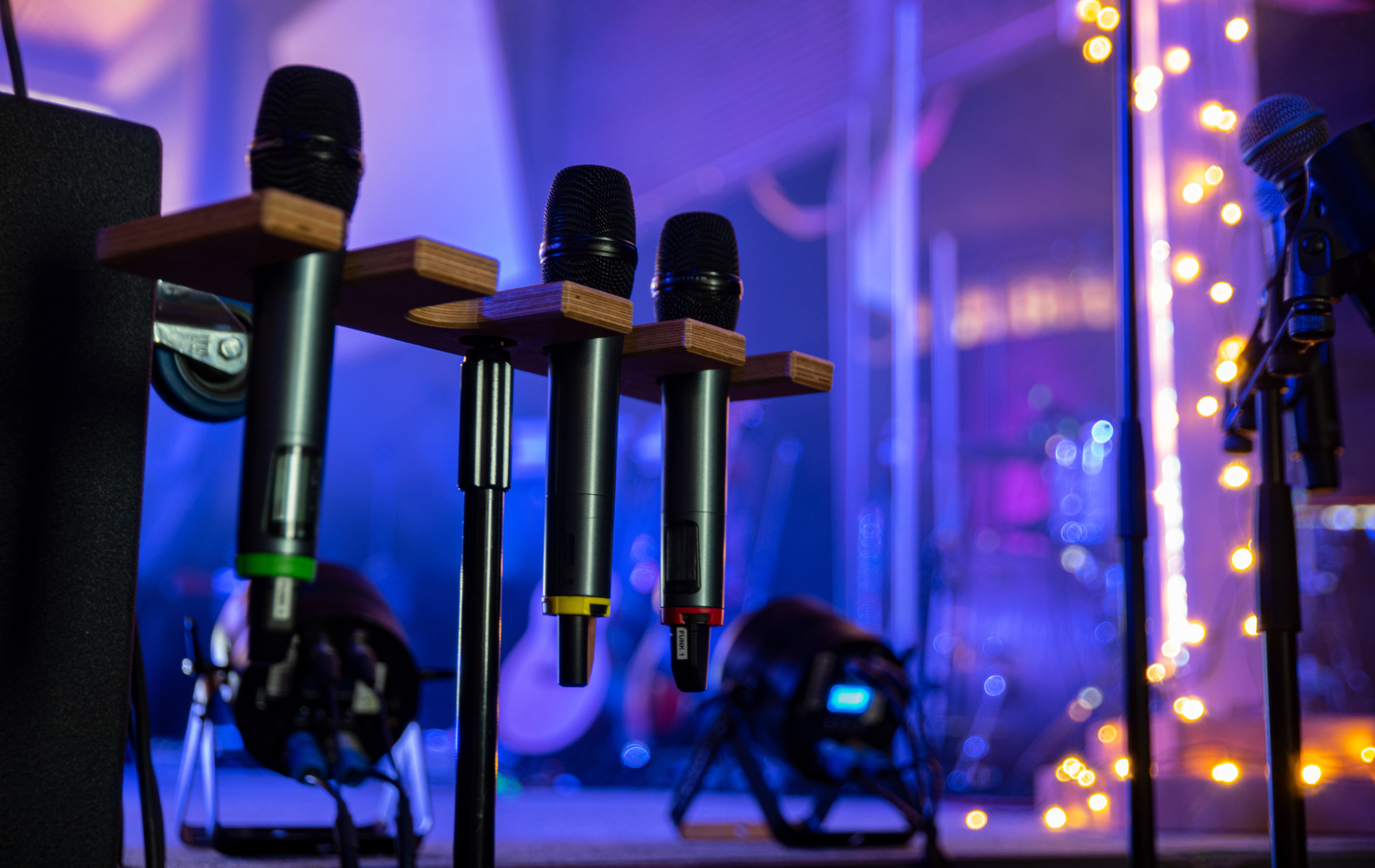 Three microphones on stands, stage background with lights, sound equipment.