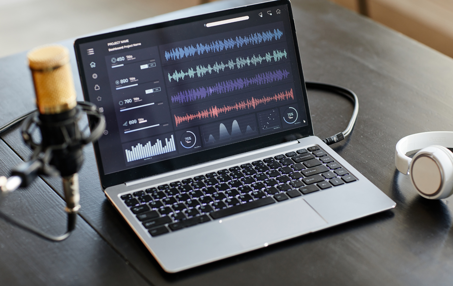 Laptop displaying audio editing software with microphone and headphones on a desk.