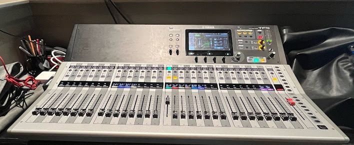 A large sound mixing console with many faders and a display screen, on a table.
