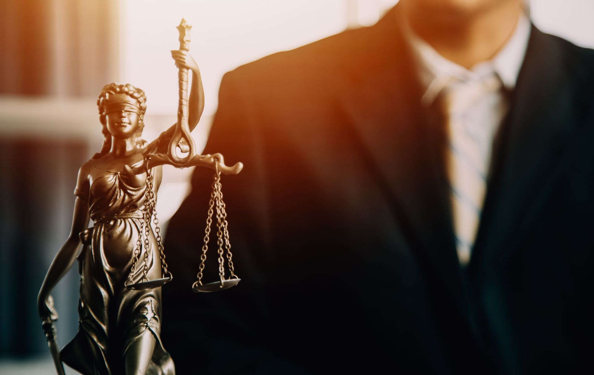 A man in a suit is standing next to a statue of justice holding scales of justice.