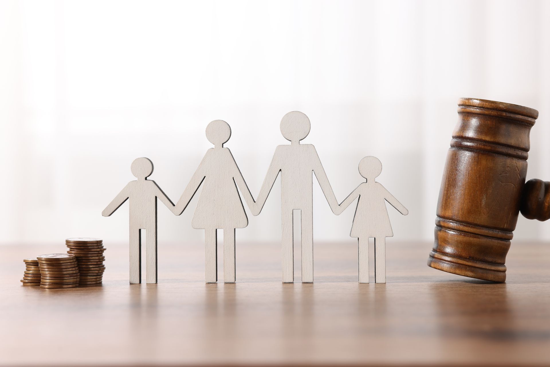 Wooden family figures holding hands beside a stack of coins and a gavel on a wooden table.