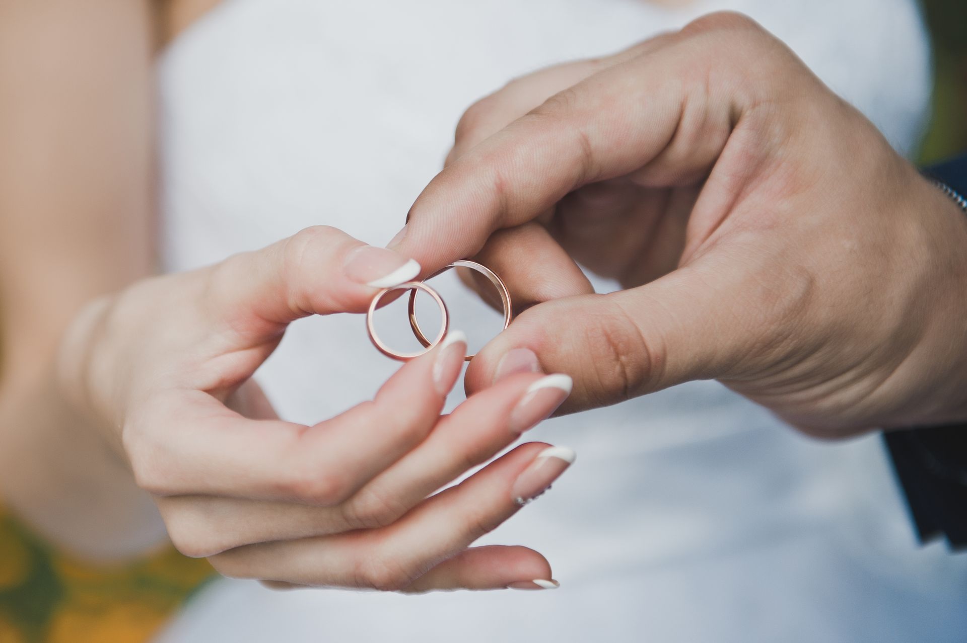 A bride and groom are holding their wedding rings in their hands.