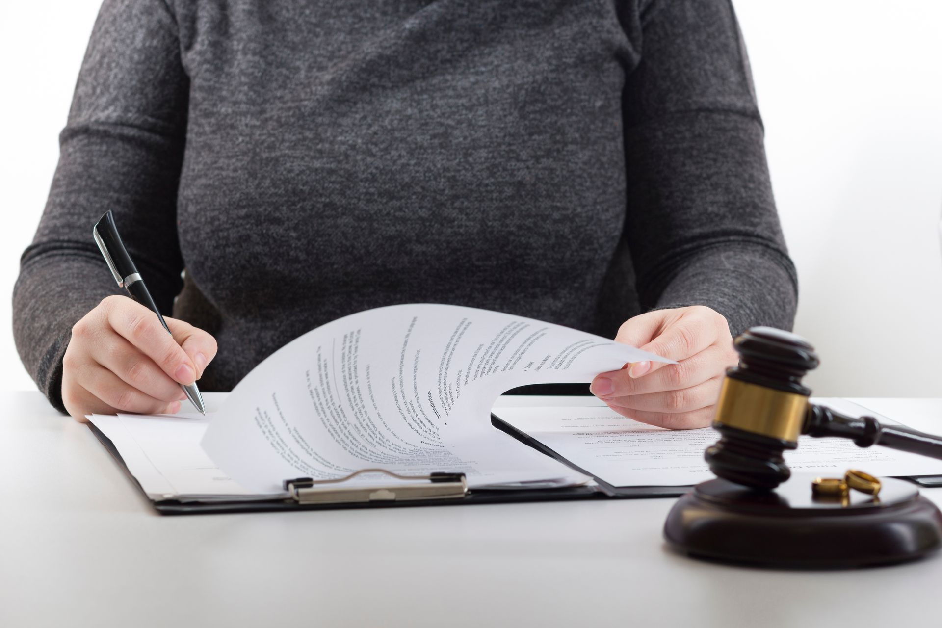 Woman writing on legal documents, gavel and wedding rings on desk.