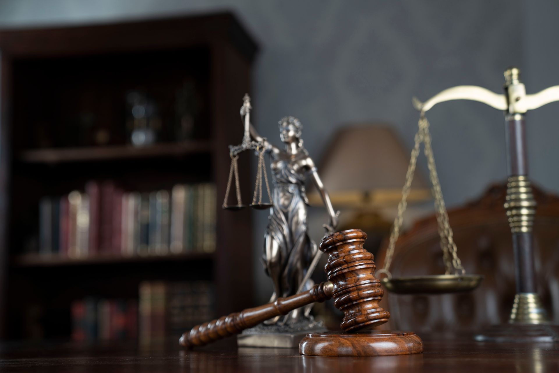 A statue of justice is sitting on a wooden table next to a wooden gavel and scales of justice.