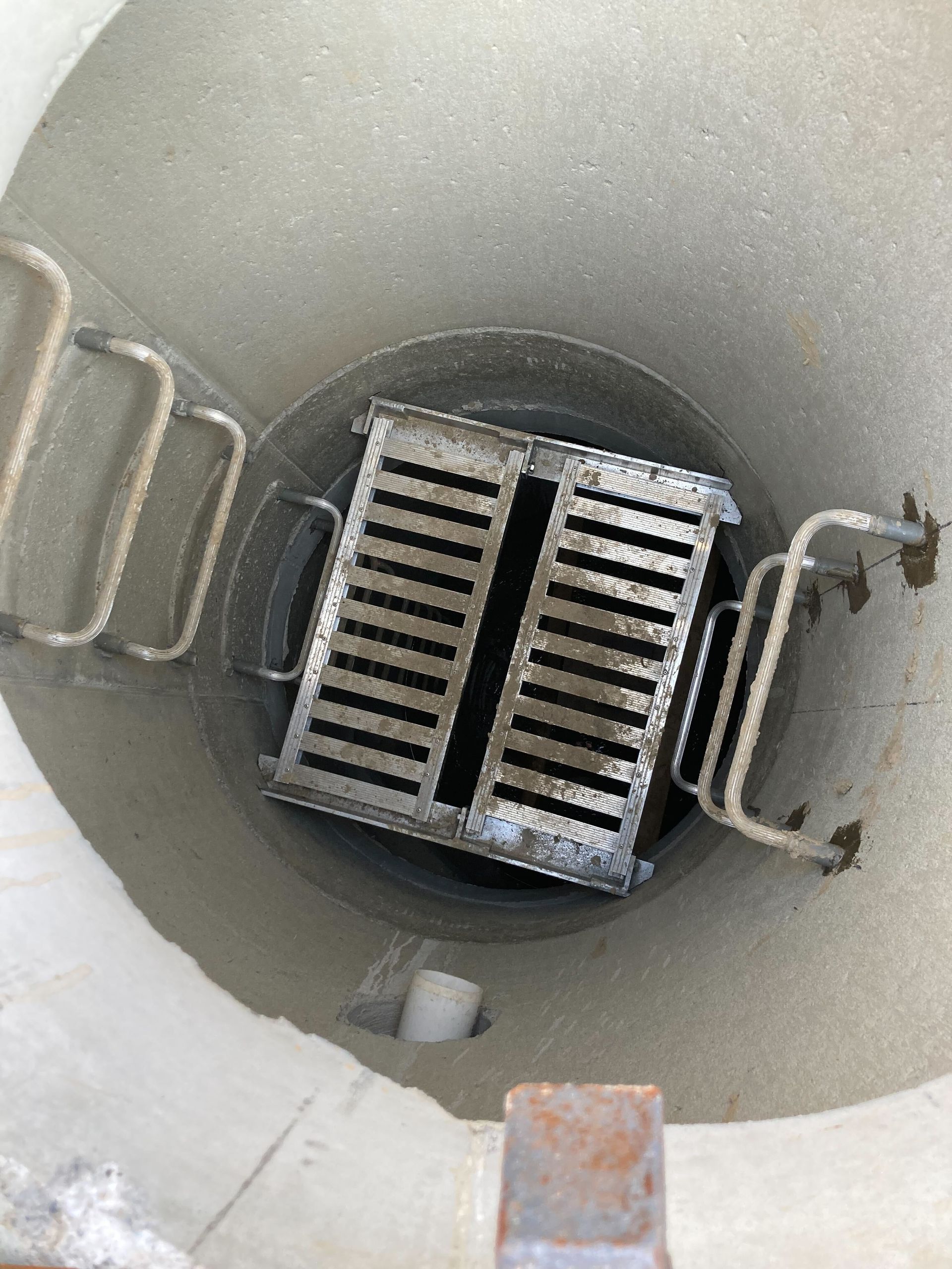 A metal drain is sitting in the middle of a concrete hole.