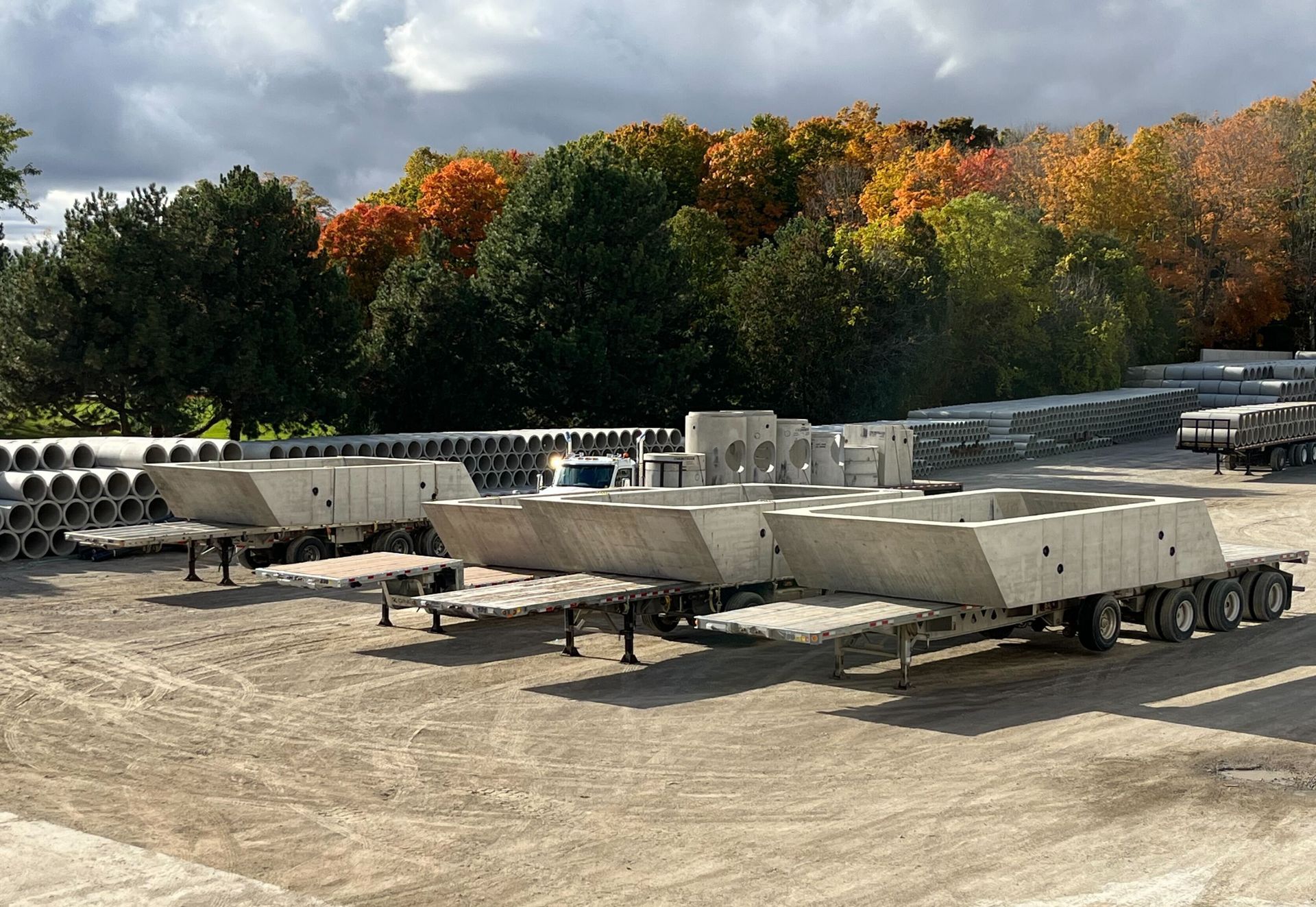 A row of trailers are parked in a dirt lot with trees in the background.