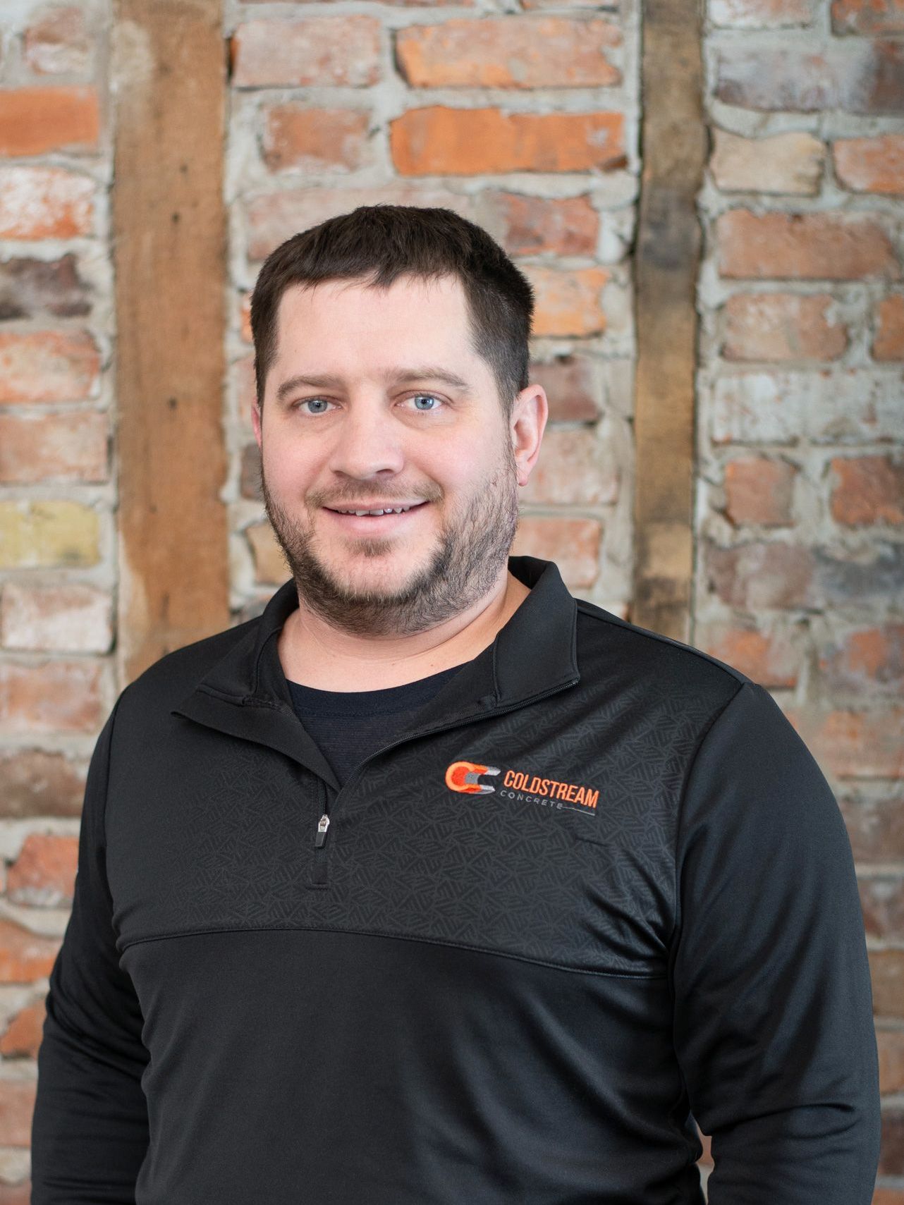A man in a black shirt is standing in front of a brick wall.