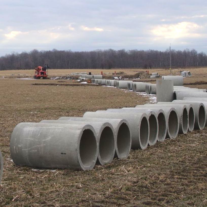 A row of concrete pipes are lined up in a field