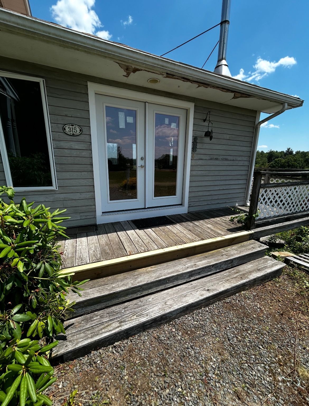 The front door of a house with a wooden deck and stairs leading up to it.