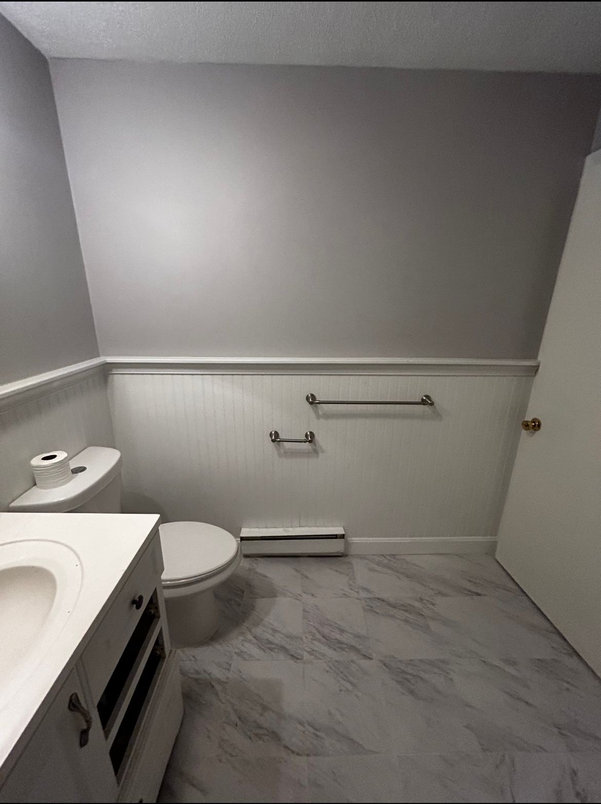 A bathroom with a toilet , sink , and towel racks.