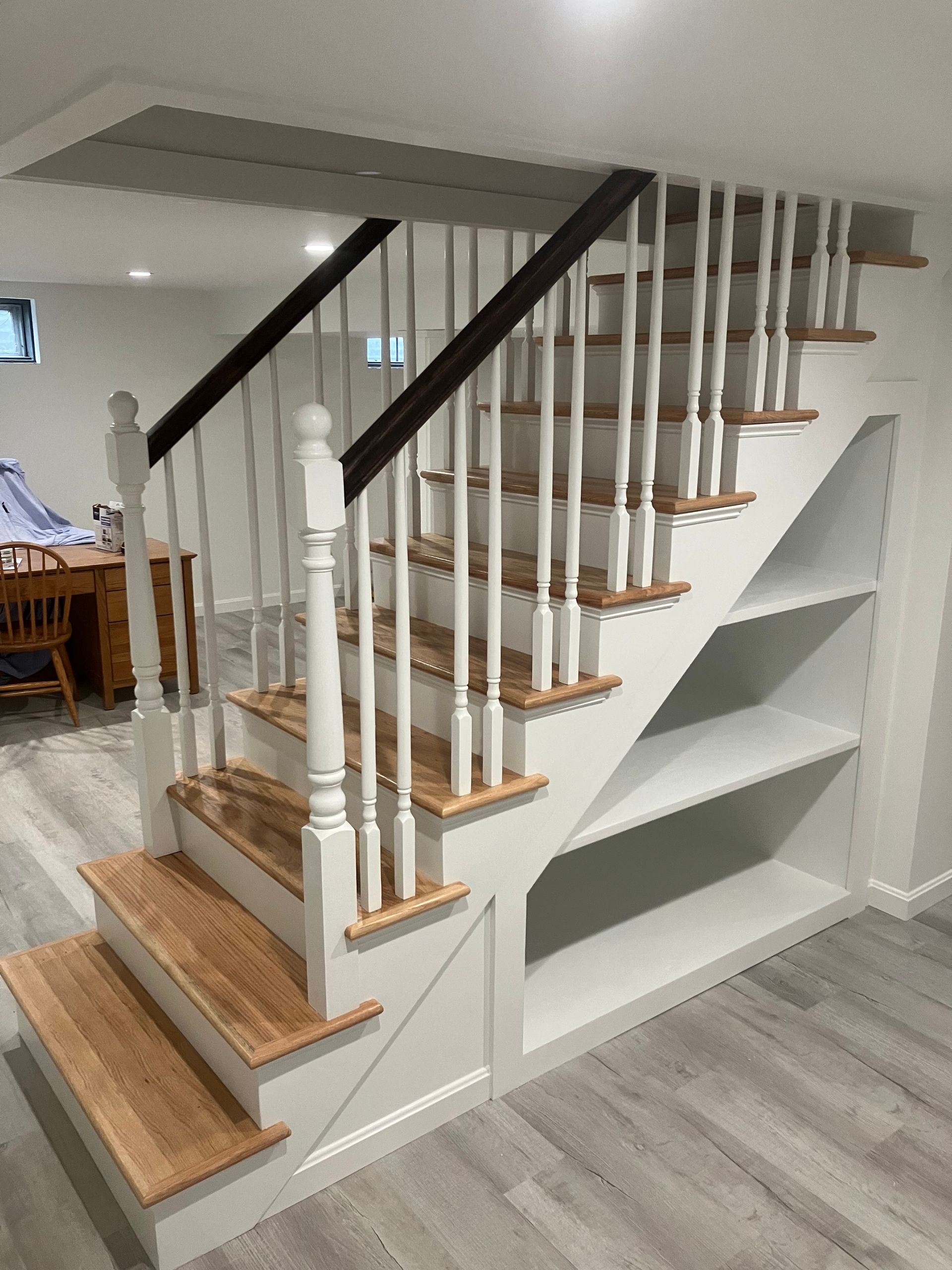 A white staircase with wooden steps and a black railing in a basement.
