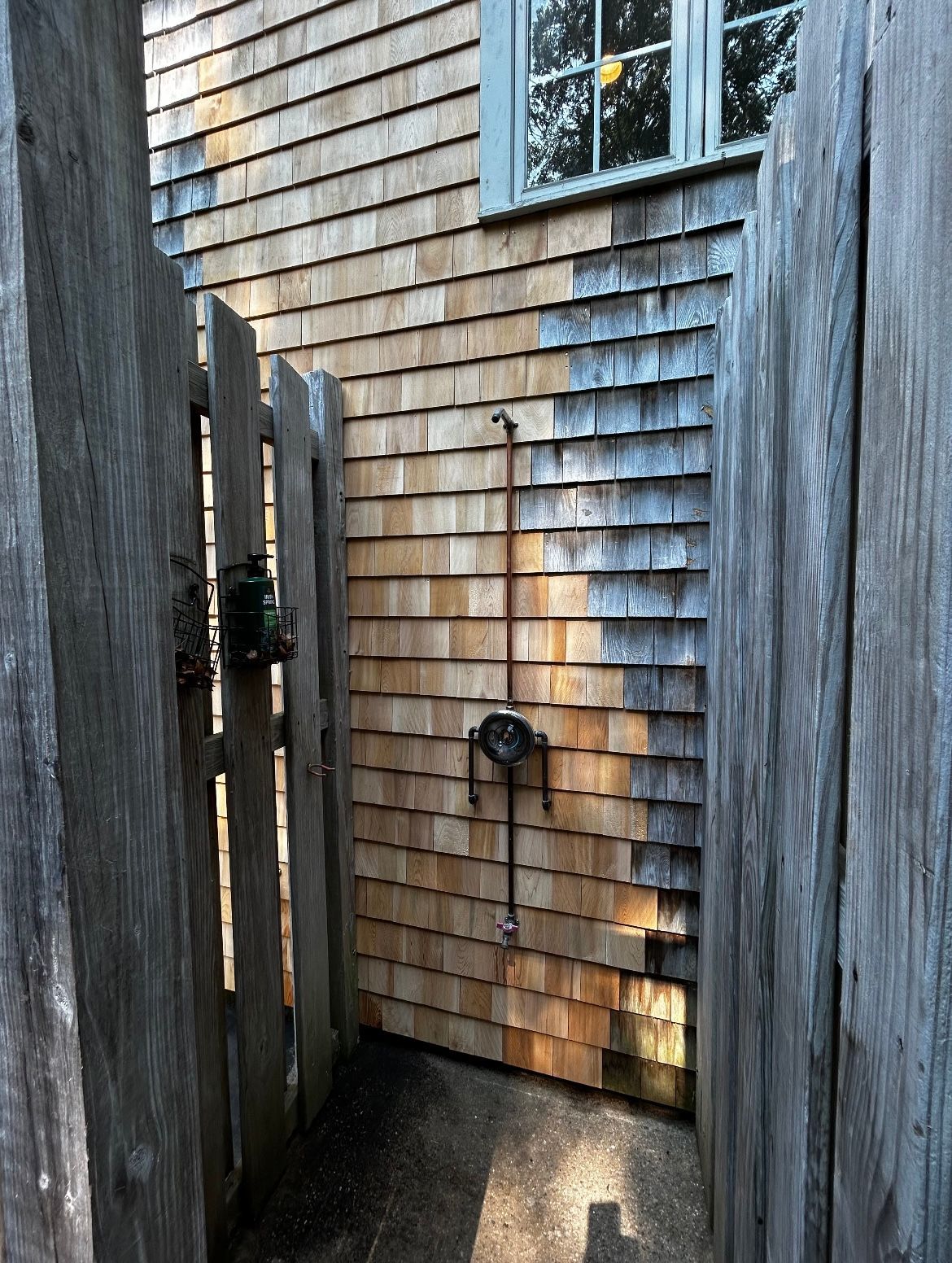 A wooden fence is leading to a wooden shower on the side of a house.