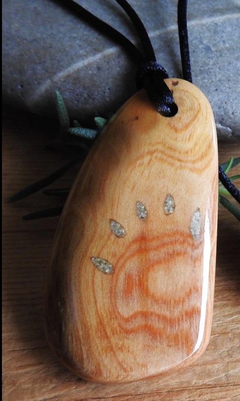 Naturally shaped and polished pendant of Douglas Fir wood with black silk necklace.  Ashes are inlaid to look like bear claw markings.