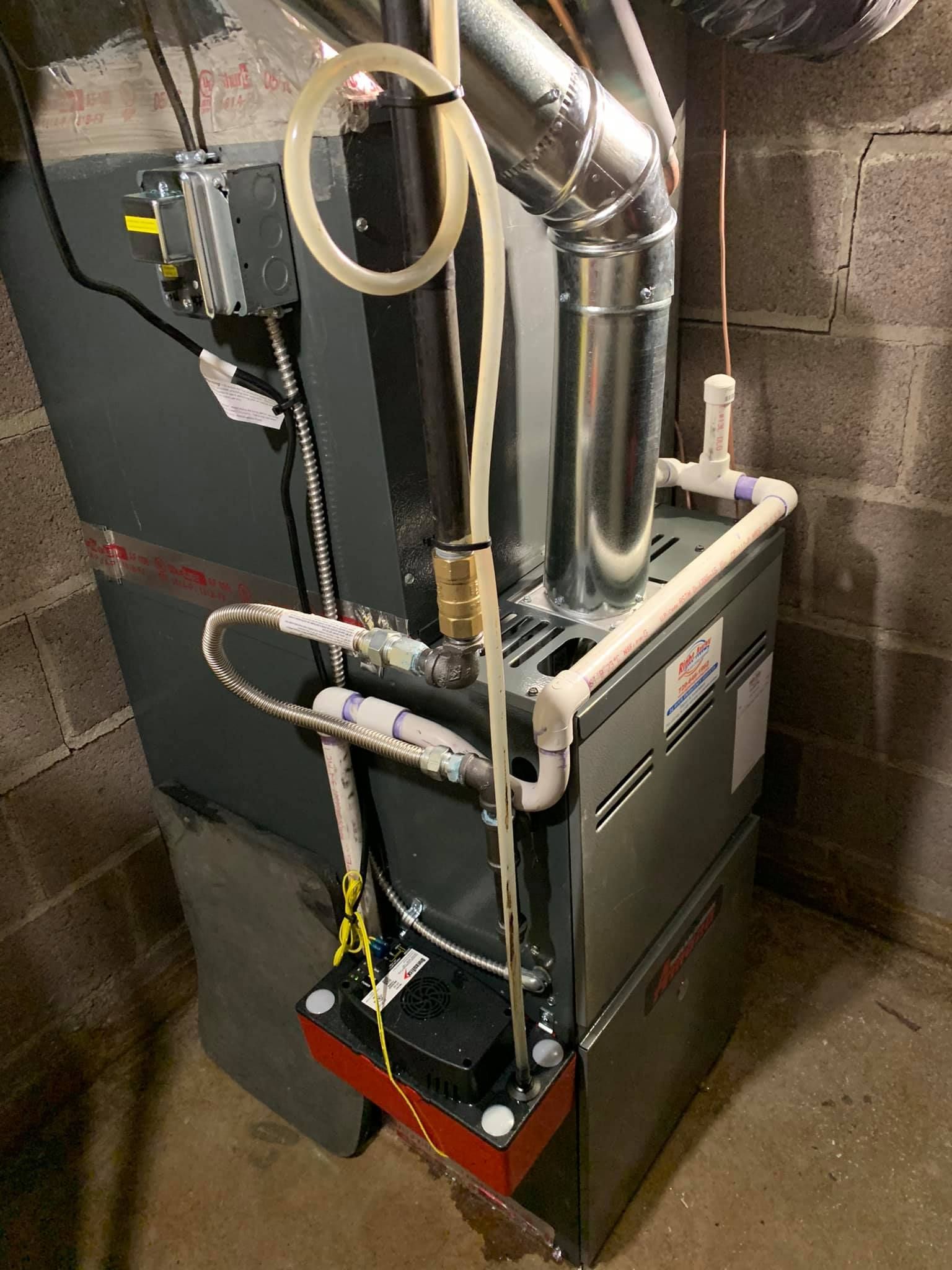 Furnace unit in a basement, with metal ductwork and various pipes.