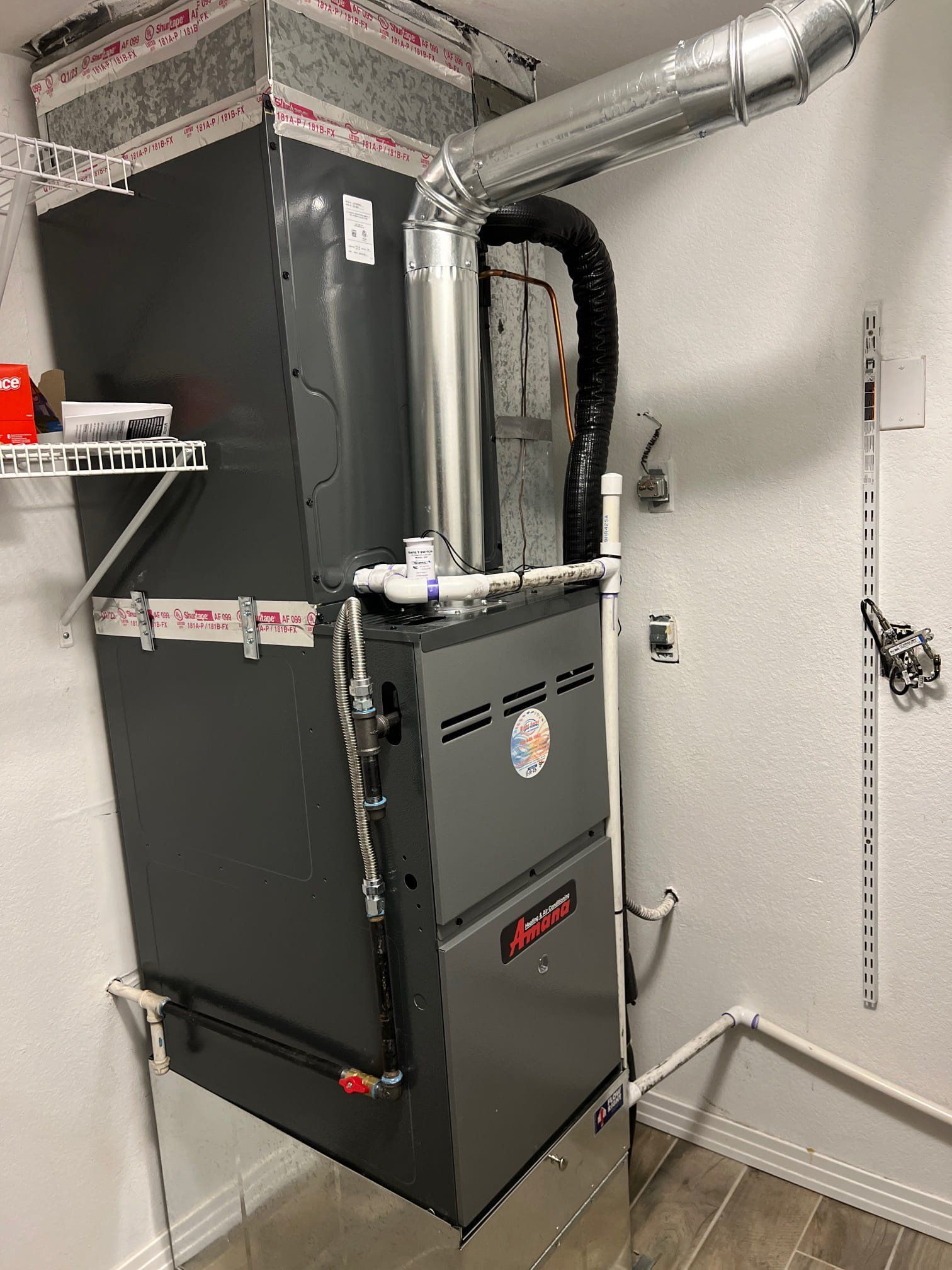 A gas furnace and attached ductwork against a white wall.