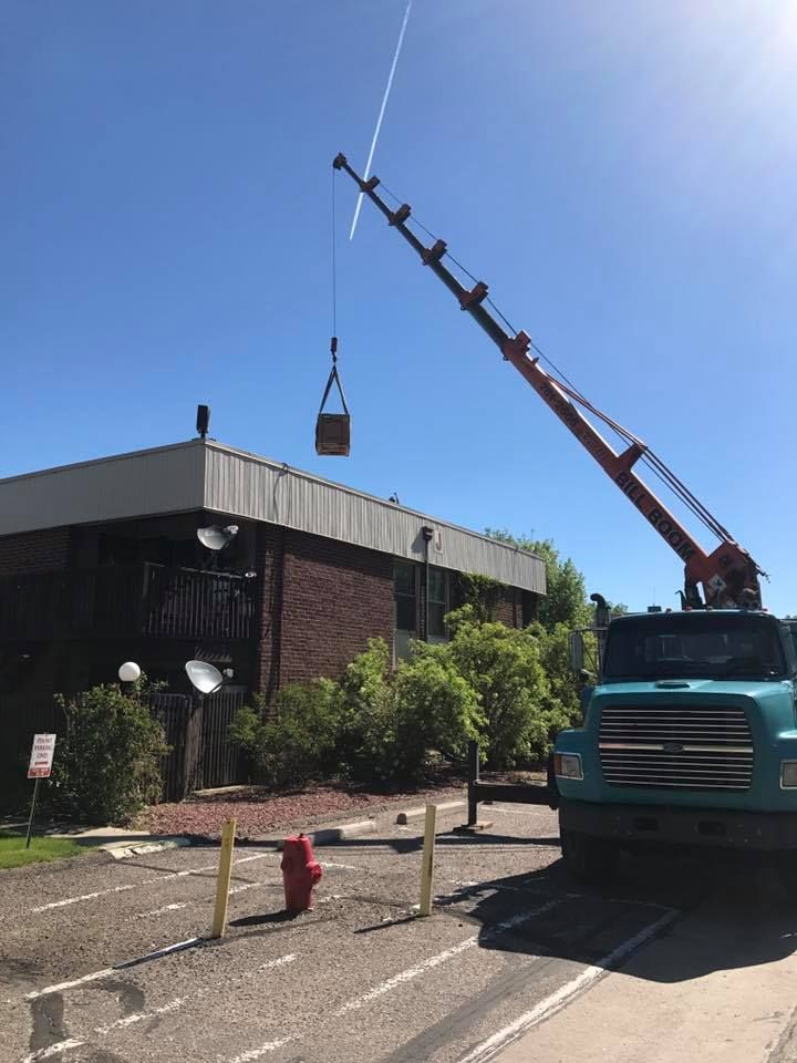 Two workers in safety vests inspect HVAC units on a rooftop, with a ladder.