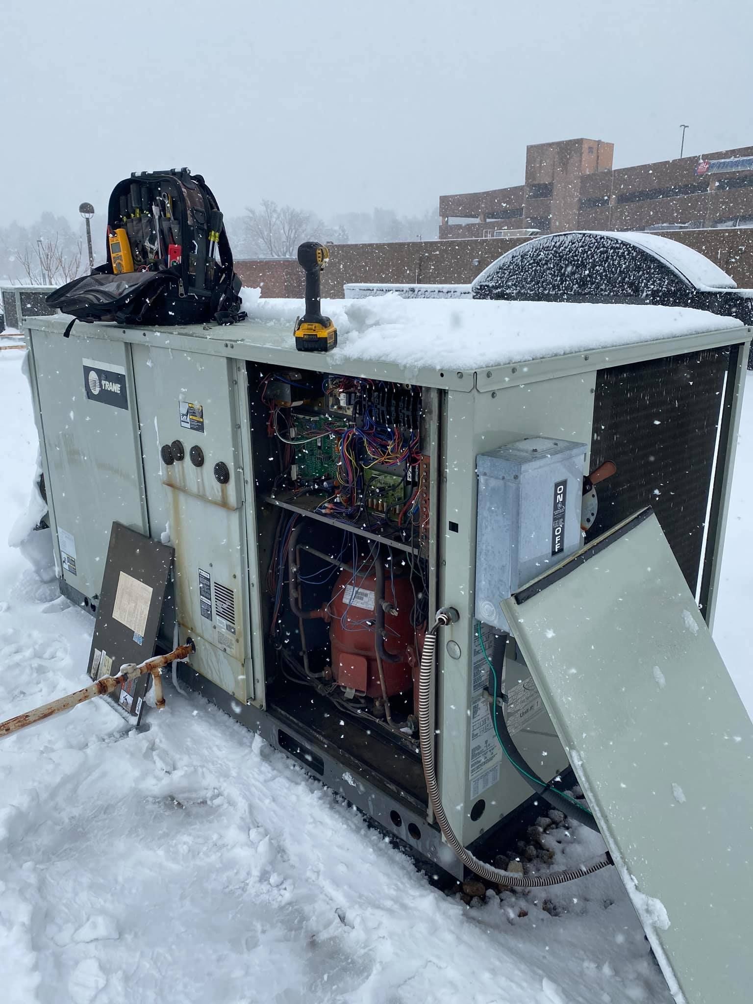 Technician in red outfit working on a white heat pump outdoors, tools nearby.