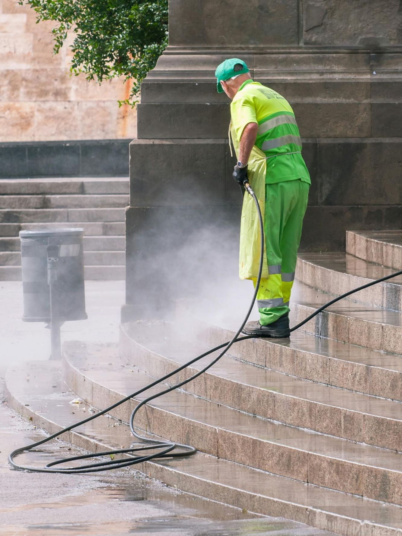 A man in green and yellow cleaning stairs with a hose