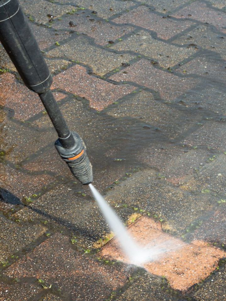 A person is using a high pressure washer to clean a brick sidewalk.