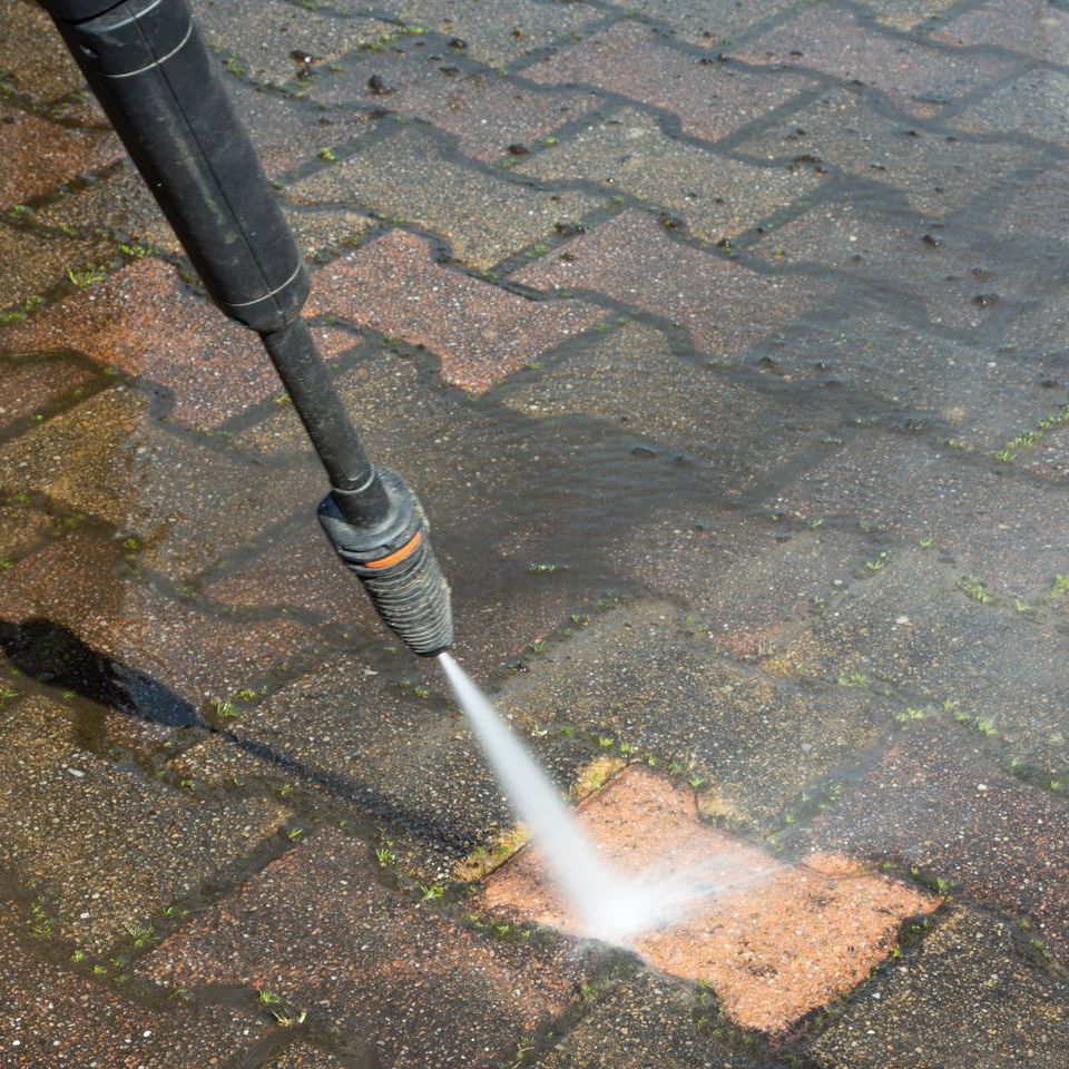 A person is using a high pressure washer to clean a brick sidewalk.