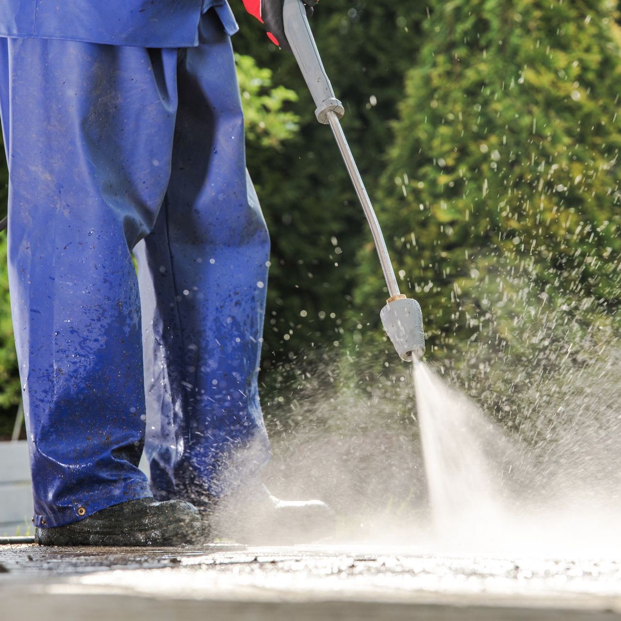 A man in blue pants is using a high pressure washer on a sidewalk.