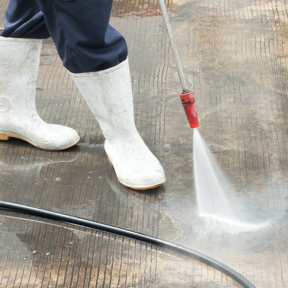 A person wearing white boots is using a high pressure washer to clean a floor