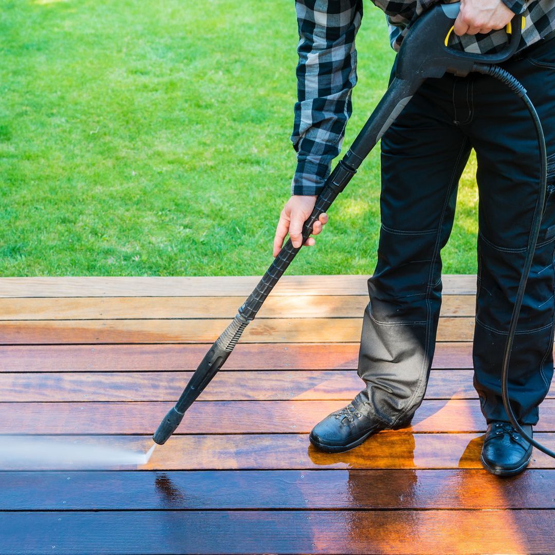 A man is using a high pressure washer to clean a wooden deck.