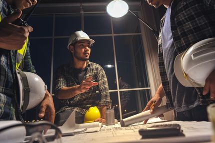 A group of construction workers are sitting around a table looking at a blueprint.