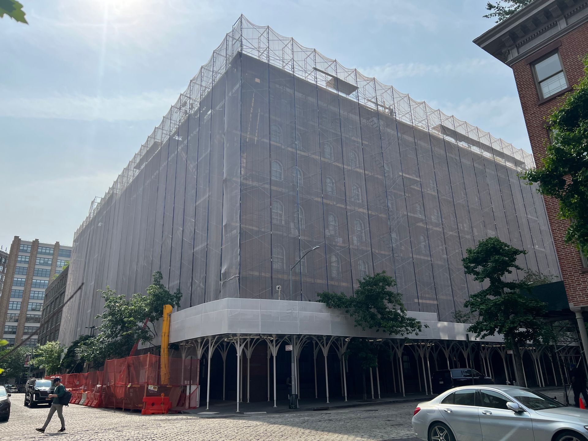 A large building is covered in scaffolding and a car is parked in front of it.